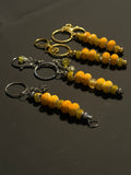 Three beaded keychains with orange and yellow marbled beads, metallic spacer beads, and split rings in gold and silver, displayed on a dark gray background.